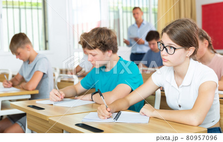 Teenage girl with glasses studying in college with classmates Teenage girl with glasses studying in college with classmates 80957096