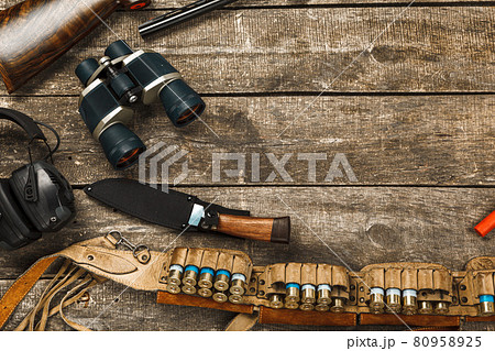 Hunting equipment on old wooden background including rifle, knife, binoculars and cartridges 80958925