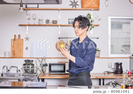 レモンを持ってキッチンに立つエプロン姿の若い男性　料理男子イメージ 80961091