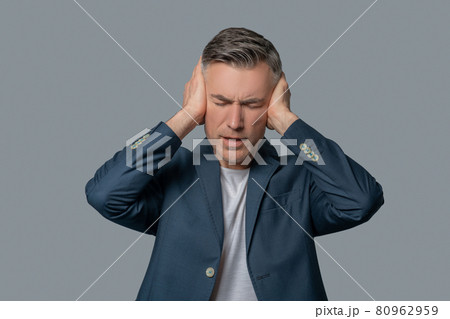 Man with drooping eyelids covering ears with hands 80962959