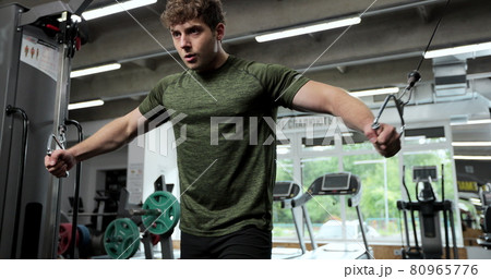 Portrait view of the man training arms with trx fitness strips in gym. Sport man with TRX straps spending time in the gym while exercising at the gym. 80965776