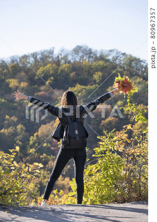 Beautiful girl on autumn park background. Girl holds bouquet of leaves and enjoys a warm day. Back view. Vertical frame 80967357