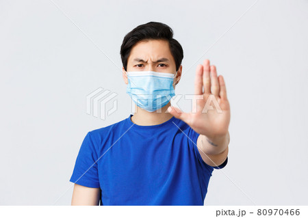 Different emotions, lifestyle and leisure during coronavirus, covid-19 concept. Angry and displeased asian man in medical mask tell to stop with stretched palm, give warning or prohibit something 80970466