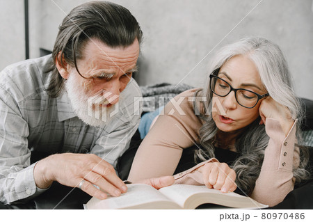 Senior couple reading book lying together on bed Senior couple reading book lying together on bed 80970486