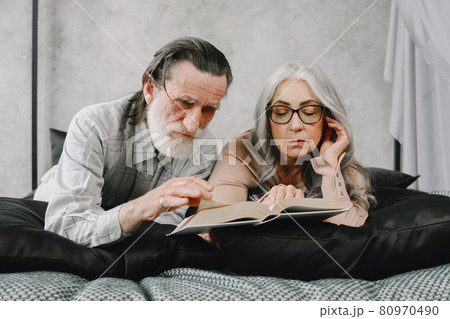 Senior couple reading book lying together on bed Senior couple reading book lying together on bed 80970490