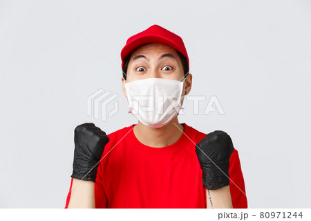 Covid-19, self-quarantine online shopping concept. Hopeful and relieved delivery guy in red cap, medical mask and gloves, fist pump achieve goal, stare amazed, received raise in courier service Covid-19, self-quarantine online shopping concept. Hopeful and relieved delivery guy in red cap, medical mask and gloves, fist pump achieve goal, stare amazed, received raise in courier service 80971244