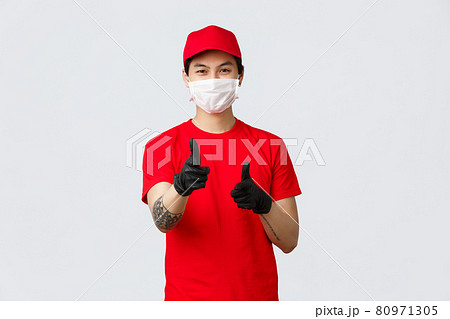 Happy delivery guy in medical mask and gloves, smiling with eyes as pointing camera, recommend carrier company service, provide fast and safe courier shipping, advertising and promoting 80971305
