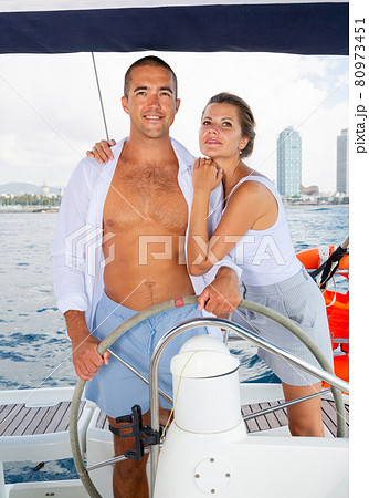 Woman and man steering yacht along shoreline of Spain Woman and man steering yacht along shoreline of Spain 80973451
