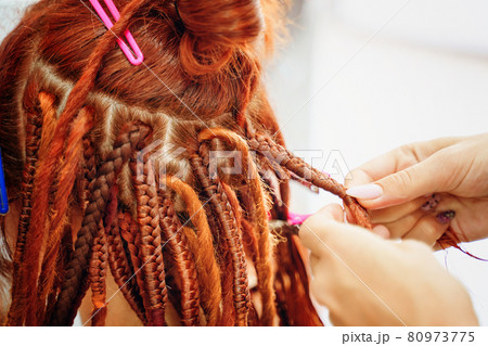 Hairdresser's hands braid girl's ginger dreadlocks. 80973775
