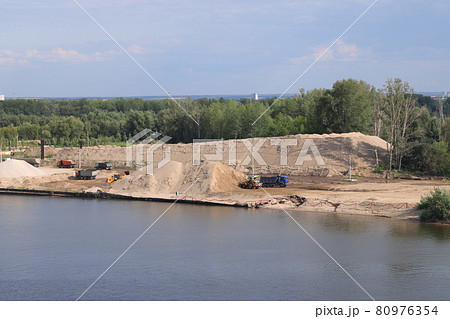 Loading soil onto trucks on a river jetty, heaps of gravel on the river bank, construction 80976354