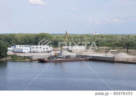Unloading a barge in a river port, gantry crane unloading crushed stone, river background Unloading a barge in a river port, gantry crane unloading crushed stone, river background 80976355