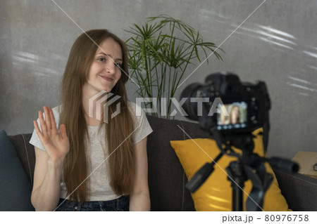 Young woman blogger takes video of herself on camera and waves her hand. Beautiful girl filming herself for vlogging Young woman blogger takes video of herself on camera and waves her hand. Beautiful girl filming herself for vlogging 80976758