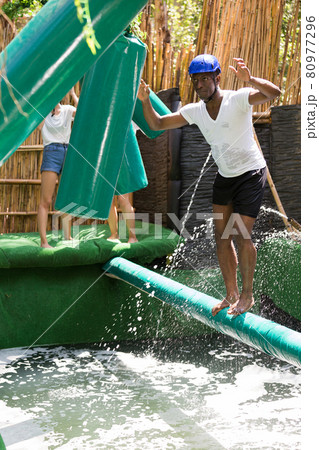 Young people try to walk the wet log in the theme park 80977296