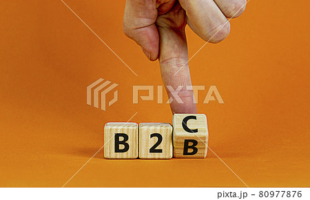 Business to Business or Busness to Consumer. Businessman turns a cube and changes words 'B2C' to 'B2B' or vice versa. Business, B2B or B2C concept. Beautiful orange background, copy space. 80977876