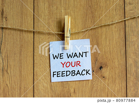 White paper with text 'we want your feedback', clip on wood clothespin. Beautiful wooden background. Business concept. Copy space. 80977884