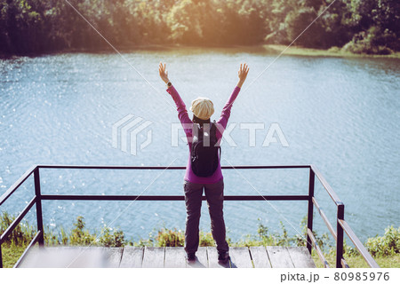 Happy backpacking woman standing with hands raise up and looking beautiful view at outdoor 80985976