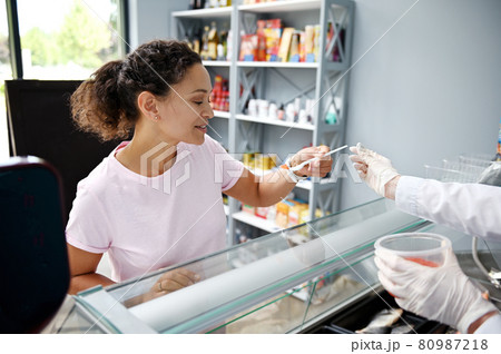 Fishmonger serving customer of fish store. Mixed race woman, purchaser tasting caviar at seafood shop. Seafood retail. Consumerism. Food and drink. 80987218