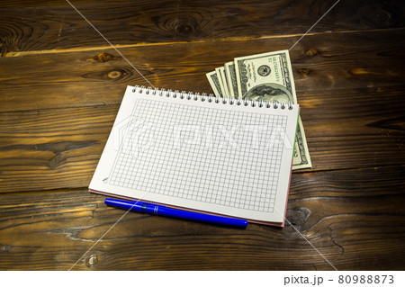 Notebook with ballpoint pen and dollar banknotes on the wooden desk 80988873