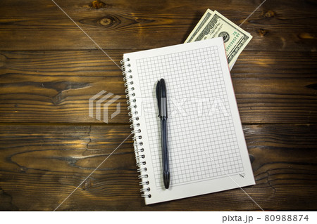 Notebook with ballpoint pen and dollar banknotes on the wooden desk 80988874