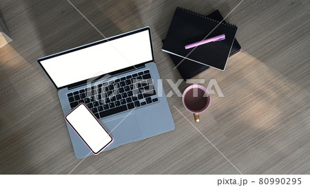 Top view of  simple workspace with blank screen laptop, mobile phone, coffee cup and notebook on wooden table. 80990295