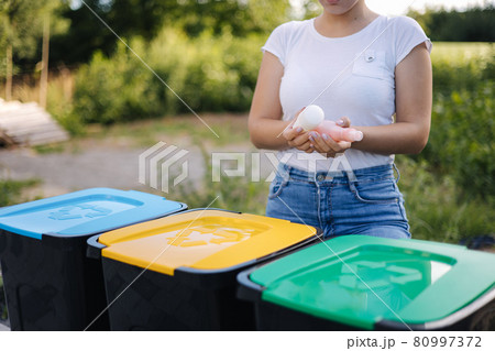 Woman throwing out in recycling bin washed and empty shampoo and deodorant bottles. Female looks at the packages to find out in wich recycling bin throw the garbage. Close-up of human hand hold trash 80997372