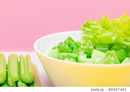 Fresh Chopped Celery Slices in White Bowl with Celery Sticks on White Cutting Board 80997465