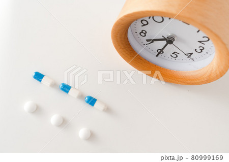 Alarm clock and white blue pills on white table background Alarm clock and white blue pills on white table background 80999169