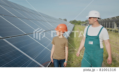 Engineer father is explaining to his little son an operation and performance of photovoltaic solar panels. Father and son happy Family concept. Boy and his dad engineer architect with safety helmets 81001316