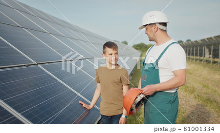 An young engineer father is explaining to his little son an operation and performance of photovoltaic solar panels at sunset. Concept: renewable energy, technology, electricity, green, future, family. An young engineer father is explaining to his little son an operation and performance of photovoltaic solar panels at sunset. Concept: renewable energy, technology, electricity, green, future, family. 81001334