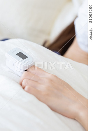 パルスオキシメーターを付けてベッドに横になる女性（顔なし） 81002200