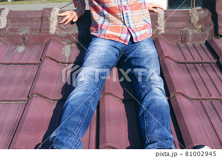 日本の赤い瓦屋根の上に座るジーンズ姿の若い男性 81002945