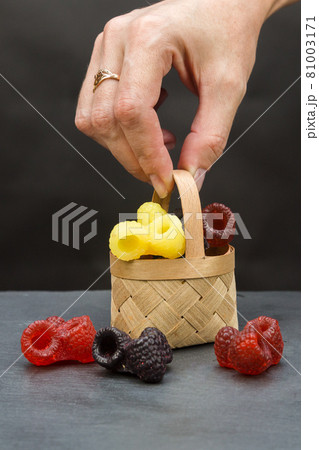A small basket with handmade soap in the form of bright berries in a woman's hand on a gray background A small basket with handmade soap in the form of bright berries in a woman's hand on a gray background 81003171
