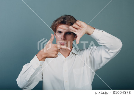 Close-up portrait of young man looking through framed hands. 81004578
