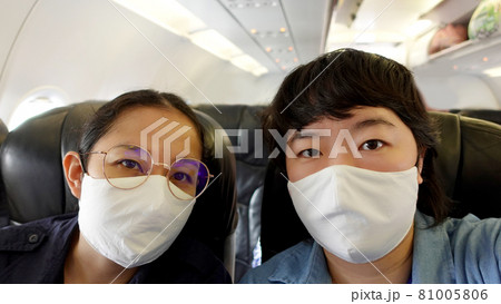 Two Asian women travel with mask on during plane flight selfie shot Two Asian women travel with mask on during plane flight selfie shot 81005806