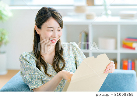 リビングでメール便の荷物を開ける若い主婦 81008869