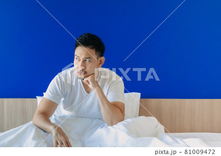 Serious and grumpy man wake up on the bed on blue space background. Serious and grumpy man wake up on the bed on blue space background. 81009472