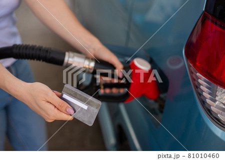 A woman fills her car with gasoline at a self-service gas station and holds a credit card A woman fills her car with gasoline at a self-service gas station and holds a credit card 81010460