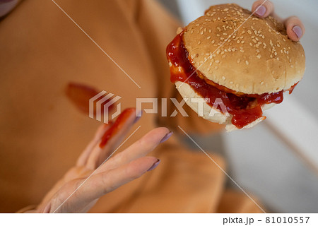 Caucasian young woman eating burger and getting dirty in ketchup. Sloppy girl Caucasian young woman eating burger and getting dirty in ketchup. Sloppy girl 81010557