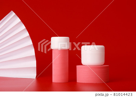 Two cream jars on pink geometric shapes for product presentation on red background with waver 81014423