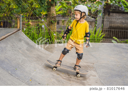 Athletic boy in helmet and knee pads learns to skateboard with in a skate park. Children education, sports Athletic boy in helmet and knee pads learns to skateboard with in a skate park. Children education, sports 81017646