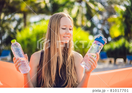 Summer lifestyle portrait of pretty girl sitting on the orange inflatable sofa selects a disposable bottle or reusable. zero waste on the beach of tropical island. Relaxing and enjoying life on air 81017701
