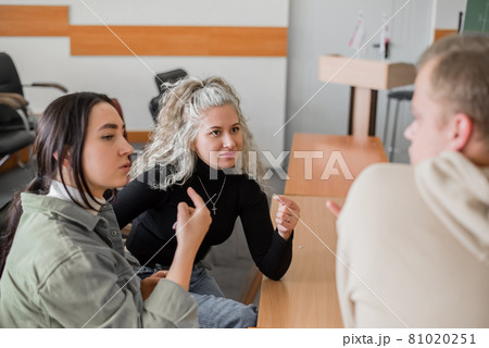 Two girls and a guy are talking in sign language. Three deaf students chatting in a university classroom. 81020251