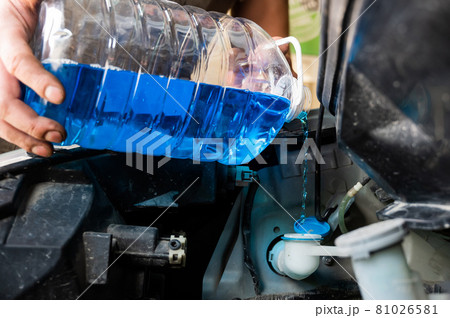 Auto mechanic pours windshield washer fluid into the car. 81026581