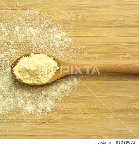 Uncooked corn flour in wooden spoon on bamboo cutting board 81029073