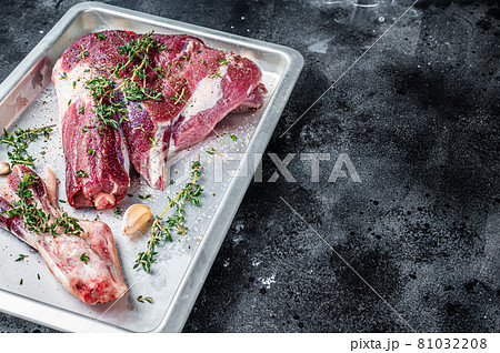 Cooking of Raw lamb mutton leg with thyme, pepper and olive oil in baking tray. Black background. Top view. Copy space 81032208