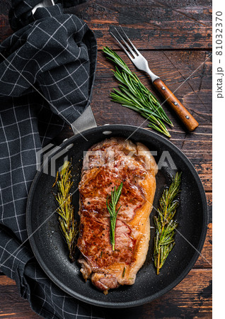 Grilled striploin beef meat steak in a pan with herbs. Dark wooden background. Top view 81032370