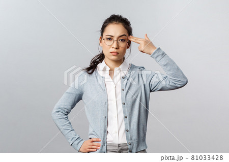 Portrait of sick and tired asian woman hear something stupid, shoot herself with finger gun as a reaction to annoying bothering conversation, staring skeptical camera, standing grey background 81033428