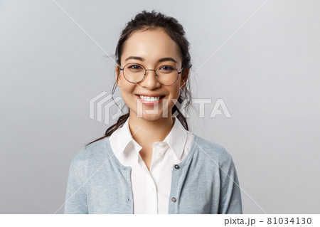 Close-up portrait of attractive, friendly-looking asian female office worker, employee or teacher in glasses, smiling broadly camera with enthusiastic attitude, stand grey background Close-up portrait of attractive, friendly-looking asian female office worker, employee or teacher in glasses, smiling broadly camera with enthusiastic attitude, stand grey background 81034130