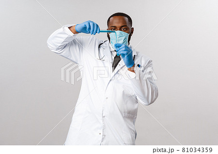Covid-19, coronavirus patient treatment and laboratory concept. Serious-looking working african-american doctor pour vaccine into test-tube, wear face-mask and latex gloves, prepare anti-flu medicine 81034359