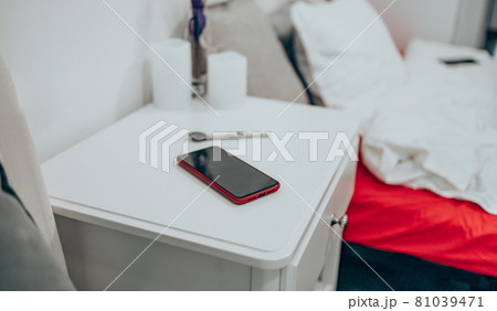 Black smartphone in a red case on the bedside table. Technology and people concept Black smartphone in a red case on the bedside table. Technology and people concept 81039471